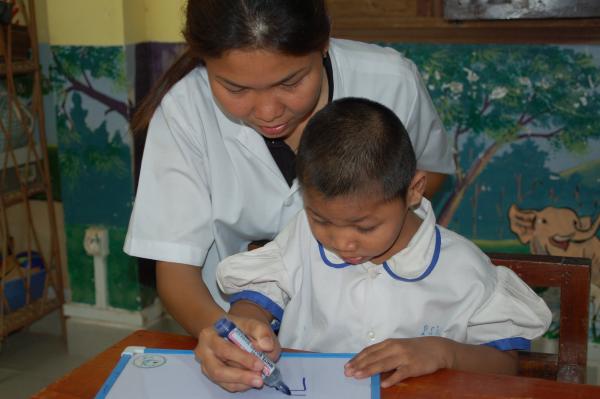 Une éducatrice spécialisée aide un enfant porteur de handicap à écrire