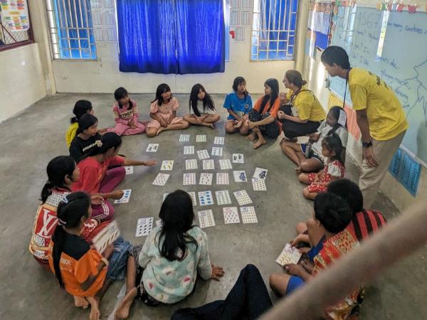 Un groupe d'enfant assis en rond dans une salle de classe font un jeux avec des images
